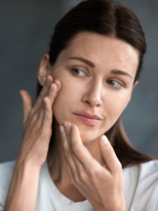 Close up unhappy woman looking at acne spots in mirror